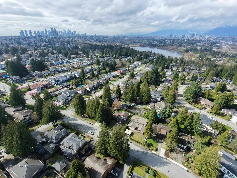 Aerial view of Buckingham Heights homes and mature trees, with Deer Lake, Burnaby towers and mountains beyond.